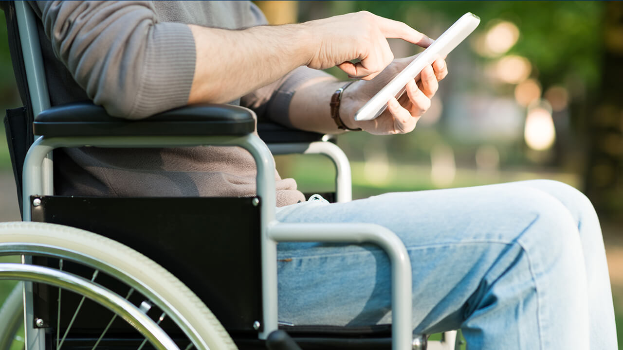 Rollstuhlfahrer mit Handy in der Hand auf Informationssuche fuer Camping mit Handicap