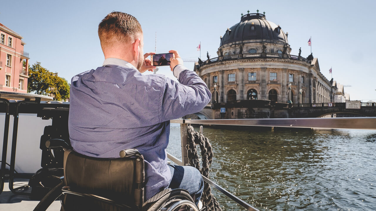 Rollstuhlfahrer fotografiert eine Sehenswuerdigkeit in Berlin mit dem Handy auf einer Reise mimt Rollstuhl