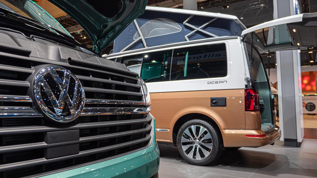 Blick an der Front eines VW California 6.1 Coast vorbei auf das Heck eines VW California 6.1. Ocean mit geöffneter Heckklappe auf dem Messestand des Caravan Salon 2019 in Düsseldorf