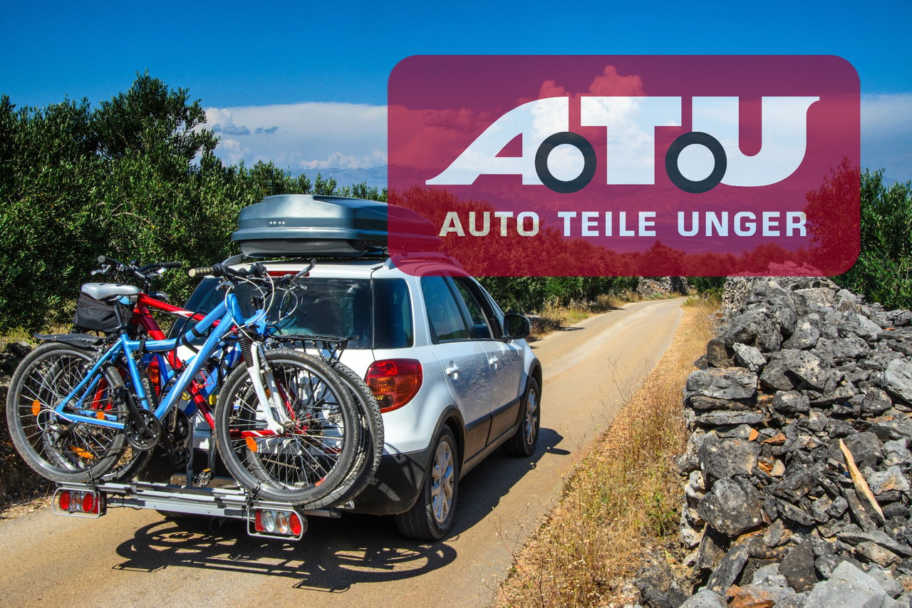 Ein Auto mit Dachbox und Fahrrädern fährt Naturstraße entlang, oben rechts ist das Logo von ATU.