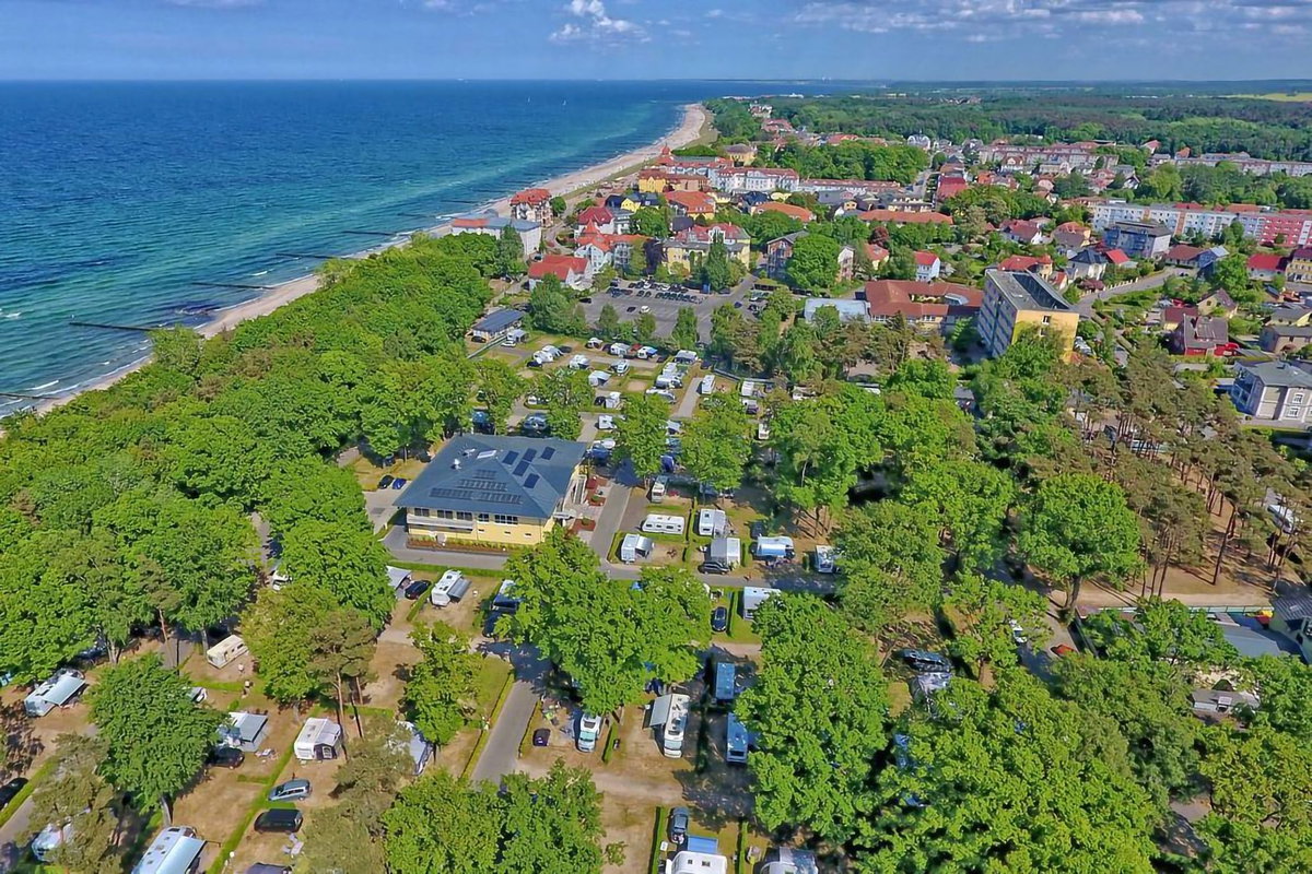 Camping.info Nr. 1 in Deutschland: Campingplatz Kühlungsborn. Zu sehen ist eine Luftaufnahme von einem Campingplatz im Grünen, im Hintergrund das Meer.